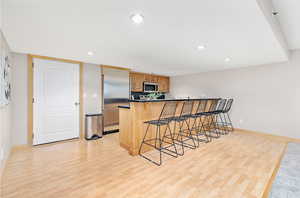 Kitchen with light hardwood / wood-style floors, kitchen peninsula, a breakfast bar area, and appliances with stainless steel finishes