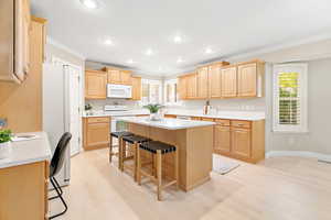 Kitchen featuring a center island, crown molding, light hardwood / wood-style floors, white appliances, and a breakfast bar