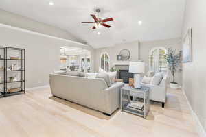 Living room with ceiling fan with notable chandelier, vaulted ceiling, light hardwood / wood-style flooring, and a healthy amount of sunlight