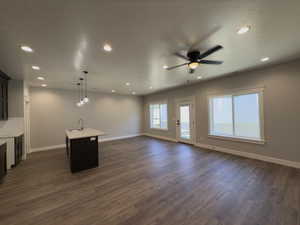 Unfurnished living room featuring wet bar, ceiling fan, dark wood-type flooring, and a textured ceiling