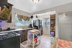 Kitchen featuring tasteful backsplash, sink, light tile patterned flooring, dark brown cabinets, and stainless steel fridge