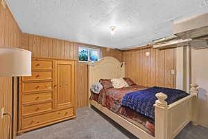 Bedroom with a textured ceiling, wooden walls, and dark carpet