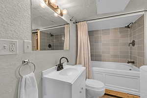 Full bathroom with vanity, shower / bath combo, a textured ceiling, and toilet