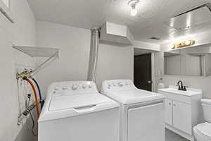 Clothes washing area with sink, a textured ceiling, and washer and clothes dryer