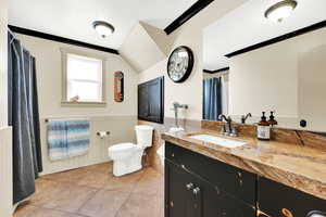 Bathroom featuring vaulted ceiling, vanity, ornamental molding, toilet, and tile patterned floors