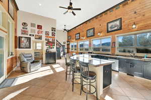 Kitchen featuring a kitchen breakfast bar, high vaulted ceiling, dishwasher, light tile patterned floors, and ceiling fan