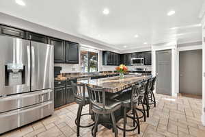 Kitchen with appliances with stainless steel finishes, dark stone countertops, a kitchen island, a breakfast bar area, and sink