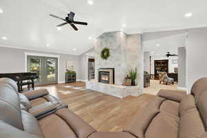 Living room with a brick fireplace, crown molding, lofted ceiling, ceiling fan, and light hardwood / wood-style flooring