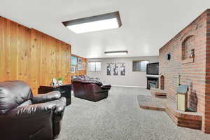 Carpeted living room with a brick fireplace and wooden walls