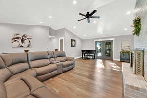 Living room with light hardwood / wood-style floors, a brick fireplace, crown molding, lofted ceiling, and ceiling fan