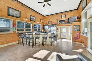 Interior space featuring crown molding, light tile patterned floors, wooden walls, and ceiling fan