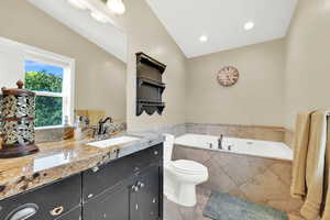 Bathroom with vaulted ceiling, vanity, a relaxing tiled tub, toilet, and tile patterned floors