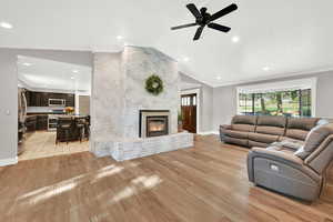 Living room with vaulted ceiling, a fireplace, light wood-type flooring, crown molding, and ceiling fan