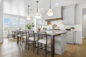 Kitchen with hanging light fixtures, decorative backsplash, custom range hood, and a center island with sink