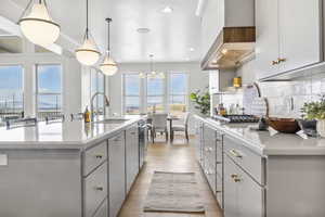 Kitchen featuring a kitchen island with sink, wall chimney range hood, pendant lighting, and sink