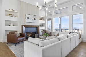 Living room featuring an inviting chandelier, a water view, a tiled fireplace, built in shelves, and light wood-type flooring