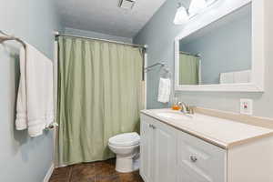 Bathroom with tile patterned flooring, a textured ceiling, toilet, vanity, and curtained shower