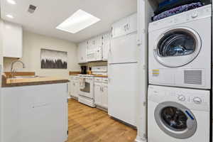 Clothes washing area with light hardwood / wood-style flooring, stacked washer and dryer, and sink