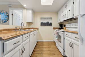 Kitchen featuring light wood-type flooring, sink, white cabinetry, white appliances, and crown molding