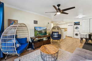 Living room featuring light hardwood / wood-style flooring, ceiling fan, stacked washer / dryer, and crown molding