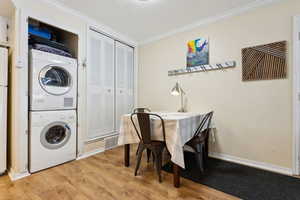 Laundry area with light hardwood / wood-style floors, stacked washing maching and dryer, and ornamental molding