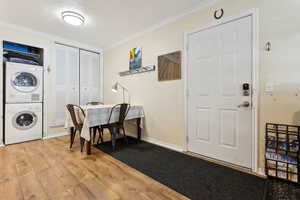 Laundry area featuring stacked washer / drying machine, light hardwood / wood-style floors, and ornamental molding