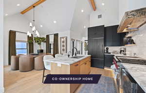 Kitchen with beam ceiling, backsplash, an island with sink, and light wood-type flooring