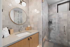 Bathroom featuring backsplash, vanity, an enclosed shower, and tile walls