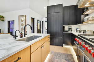 Kitchen featuring vaulted ceiling, backsplash, light stone countertops, light hardwood / wood-style flooring, and sink