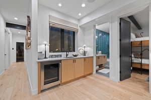 Interior space with light brown cabinetry, beverage cooler, sink, beam ceiling, and light hardwood / wood-style floors