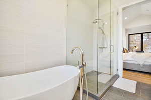 Bathroom featuring shower with separate bathtub, lofted ceiling, and tile patterned flooring