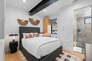 Bedroom featuring ensuite bath, beamed ceiling, and light wood-type flooring