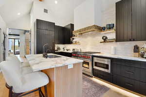 Kitchen featuring appliances with stainless steel finishes, an island with sink, high vaulted ceiling, light wood-type flooring, and a kitchen bar