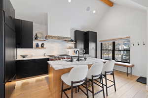 Kitchen with decorative backsplash, sink, light hardwood / wood-style floors, and an island with sink