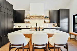 Kitchen with backsplash, a center island with sink, a breakfast bar area, and light hardwood / wood-style flooring