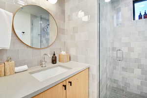 Bathroom with decorative backsplash, tile walls, a shower with door, and vanity