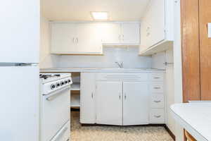 Kitchen featuring decorative backsplash, white appliances, white cabinetry, and sink