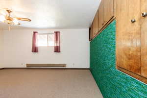 Carpeted spare room with ceiling fan, baseboard heating, and a textured ceiling