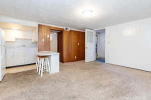 Basement with wood walls, white refrigerator, light colored carpet, and sink