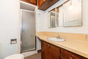 Bathroom featuring a shower with door, vanity, and toilet