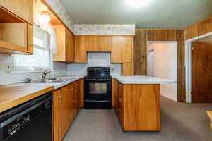 Kitchen featuring sink, wood walls, kitchen peninsula, light carpet, and black appliances