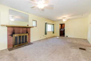 Unfurnished living room featuring carpet, ceiling fan, and a brick fireplace