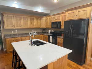 Kitchen with brand new quartz countertop on the island, hardwood flooring, black appliances, and a kitchen breakfast bar