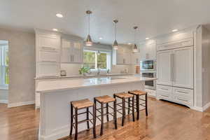 Kitchen featuring double oven, a kitchen island, light hardwood / wood-style flooring, and white cabinetry