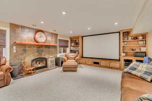 Home theater projection room featuring built in shelves, a fireplace, crown molding, and carpet flooring