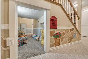 Kids playroom underneath the stairs with a textured ceiling and carpet flooring