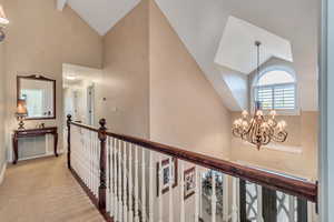 Hall featuring light colored carpet, an inviting chandelier, beamed ceiling, and high vaulted ceiling