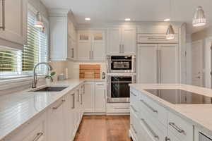 Kitchen featuring black electric cooktop, sink, white cabinets, hanging light fixtures, and double oven