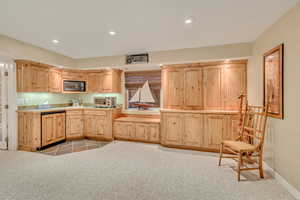 Kitchen featuring black microwave, light brown cabinets, light carpet, and paneled dishwasher