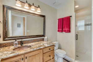 Bathroom with vanity, toilet, a shower with door, and tasteful backsplash